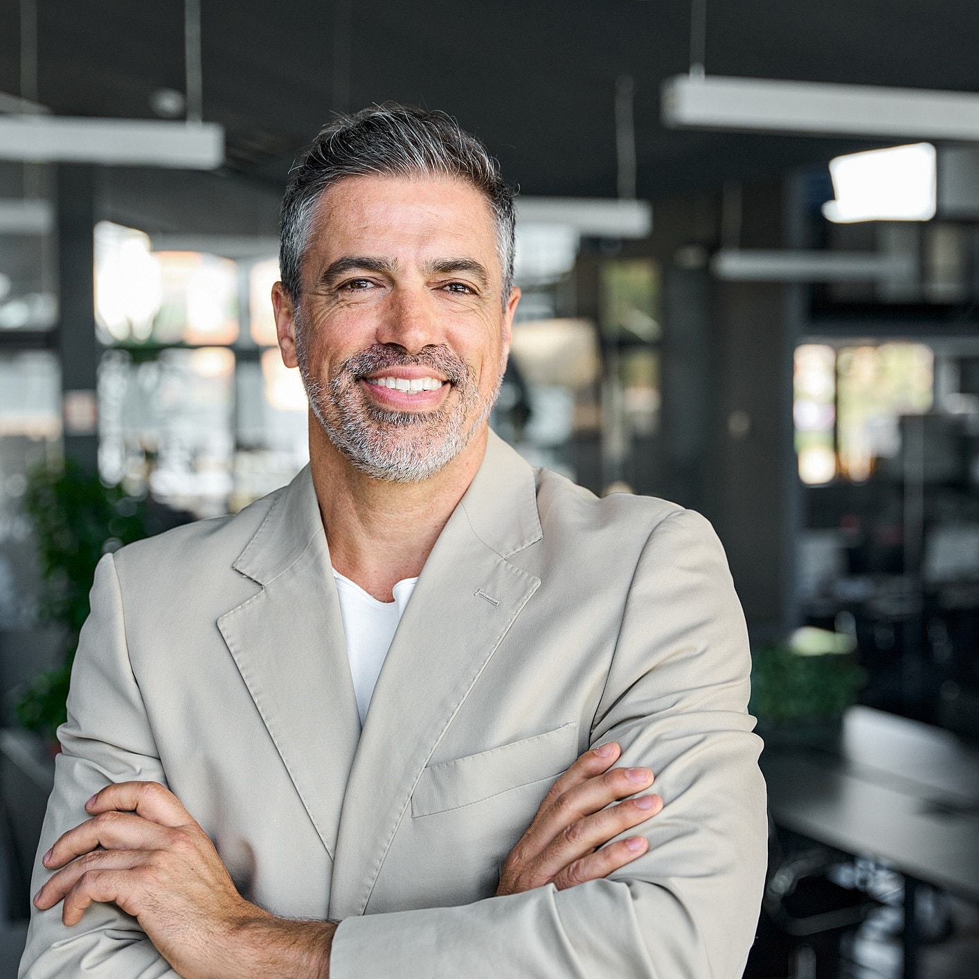 Smiling man in modern office setting, arms crossed.