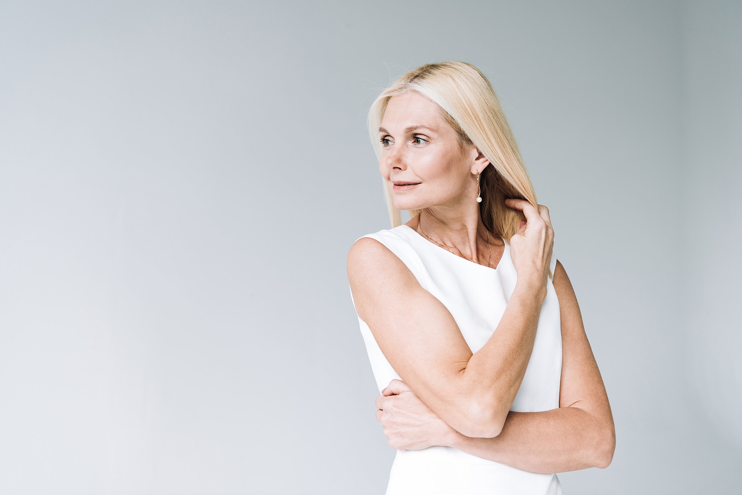 Elegant woman in white dress touching her hair.