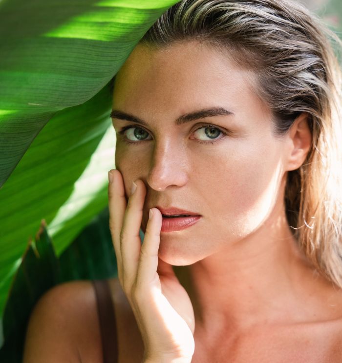 Newport Beach facial plastic surgery model with hand on face, surrounded by leaves.