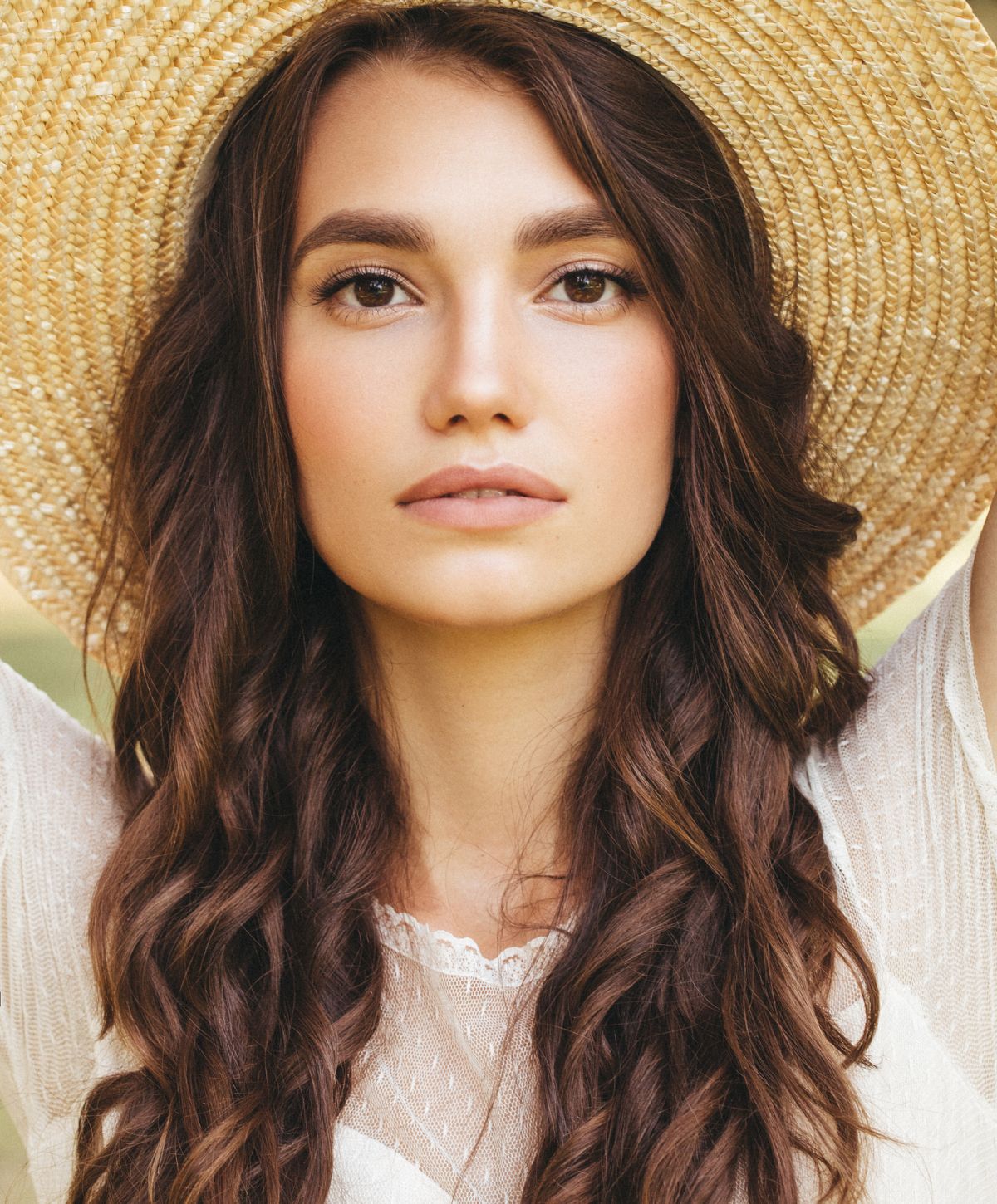 Newport Beach neck lift model in a straw hat with long, wavy hair.