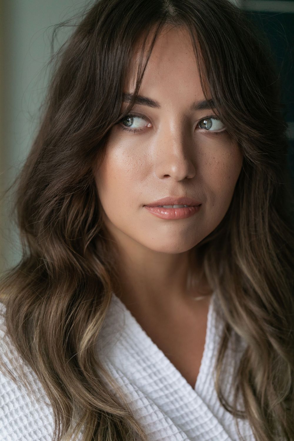 Newport Beach facial plastic surgery model with long hair wearing a robe, looking thoughtfully.