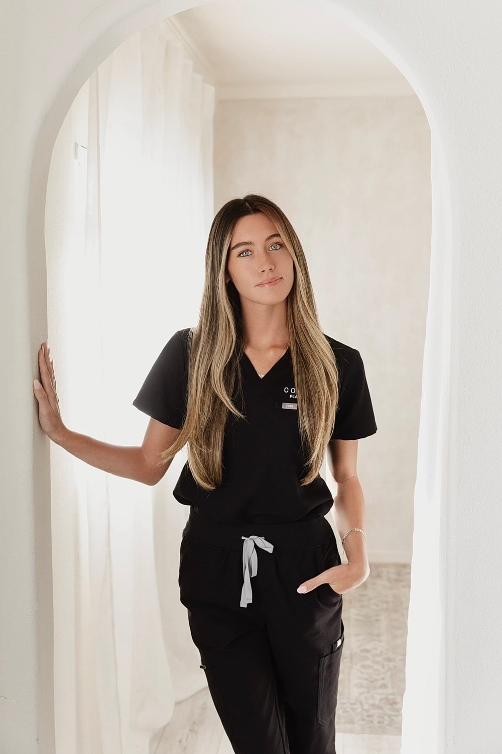 Woman in scrubs standing by an archway.