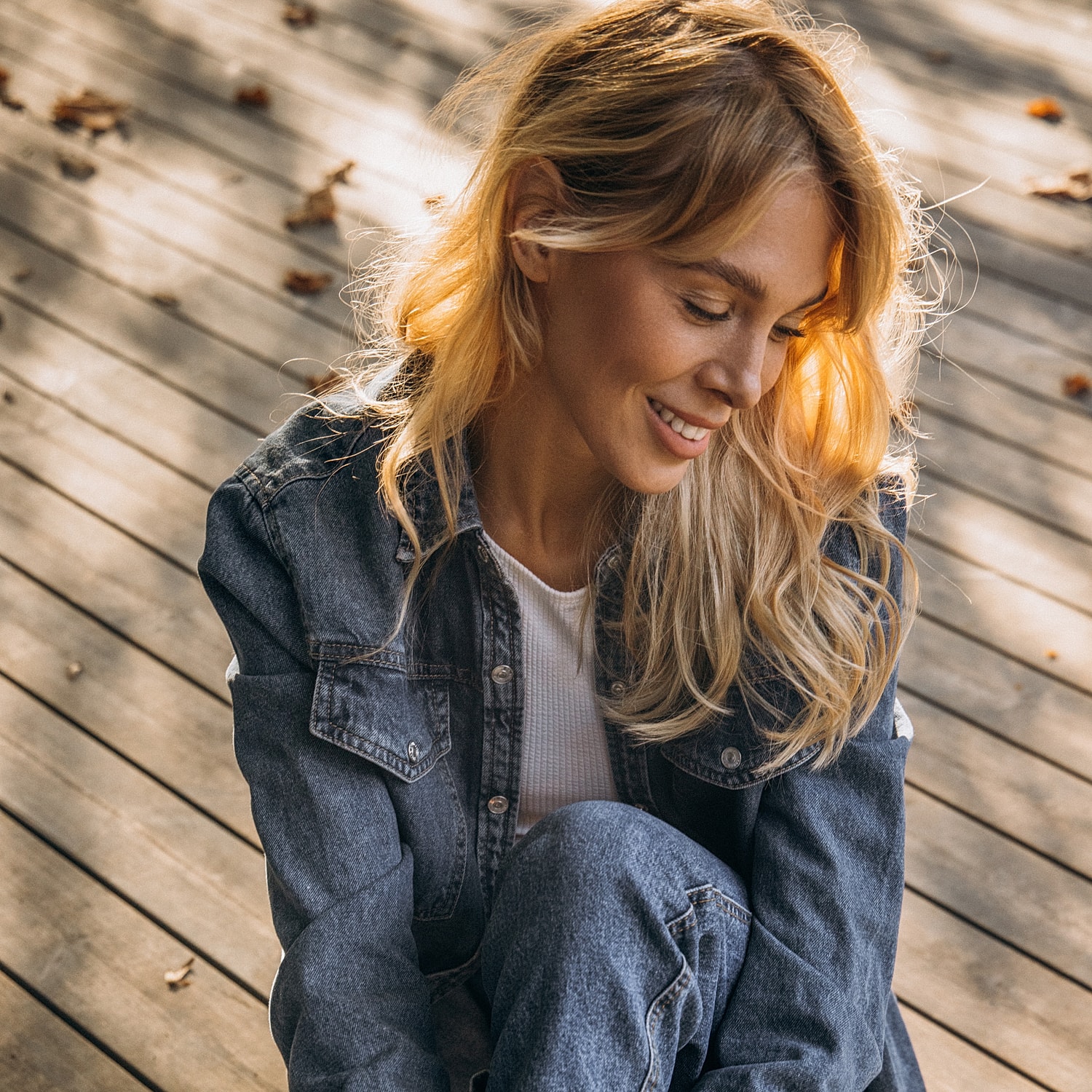 Smiling woman in denim outfit on wooden patio.