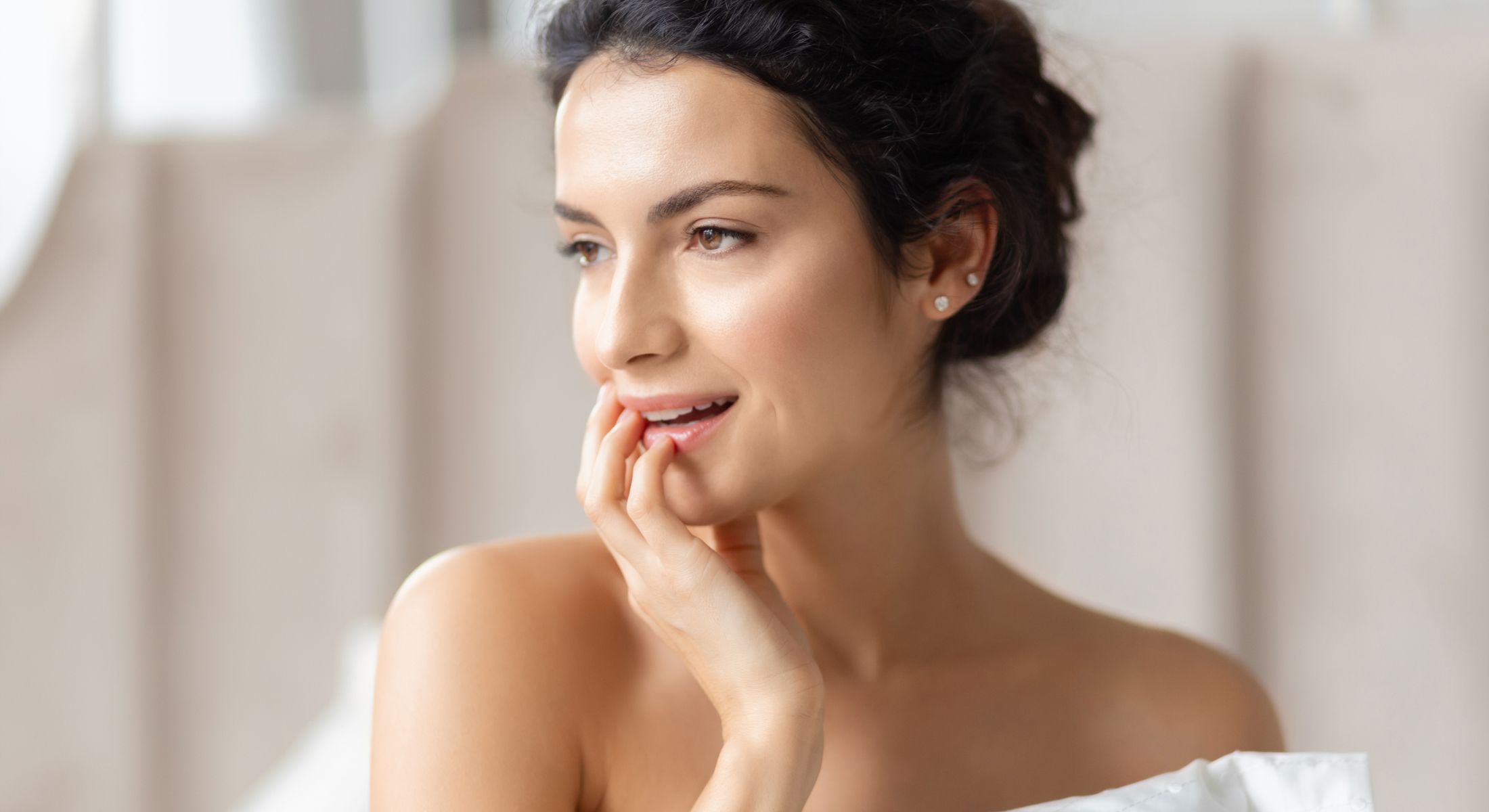 Newport Beach primary rhinoplasty model smiling with hand on her face.